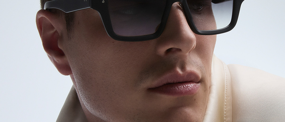 Man wearing large black sunglasses and a light-colored jacket against a plain background. “DITA” is written across the bottom in white text.