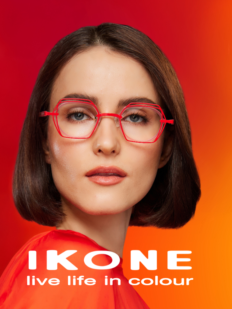 Woman with straight brown hair wears red-framed glasses and an orange top. Text below reads: "IKONE live life in colour" on a red-orange gradient background.