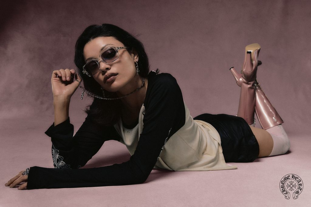 A person wearing sunglasses and a raglan shirt lies on their stomach, wearing tall, pale pink boots with high heels.