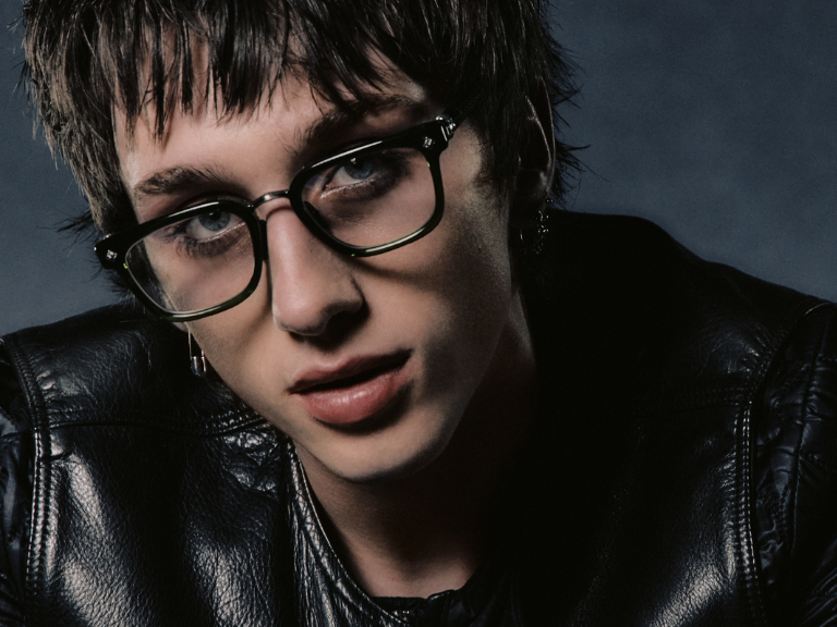 Portrait of a person with short dark hair wearing glasses and a black leather jacket.