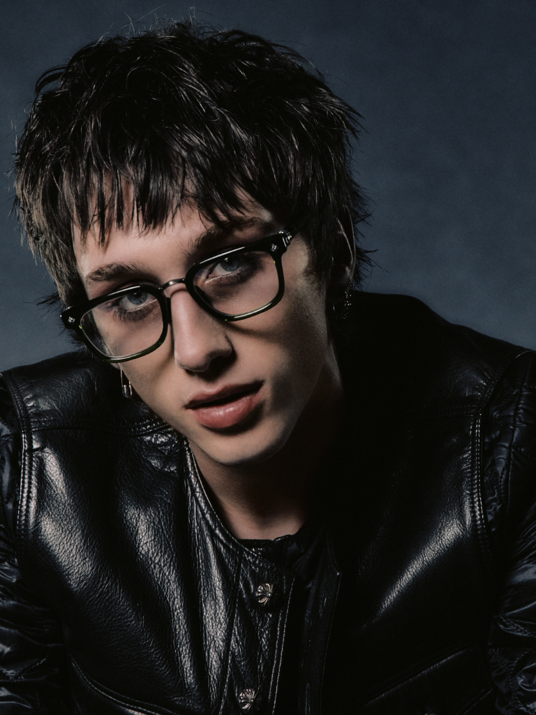 Portrait of a person with short dark hair wearing glasses and a black leather jacket.
