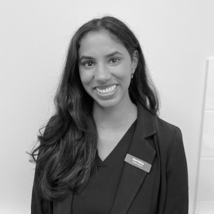 A woman with long dark hair smiling, wearing a blazer with a name tag that reads “Danisha.”