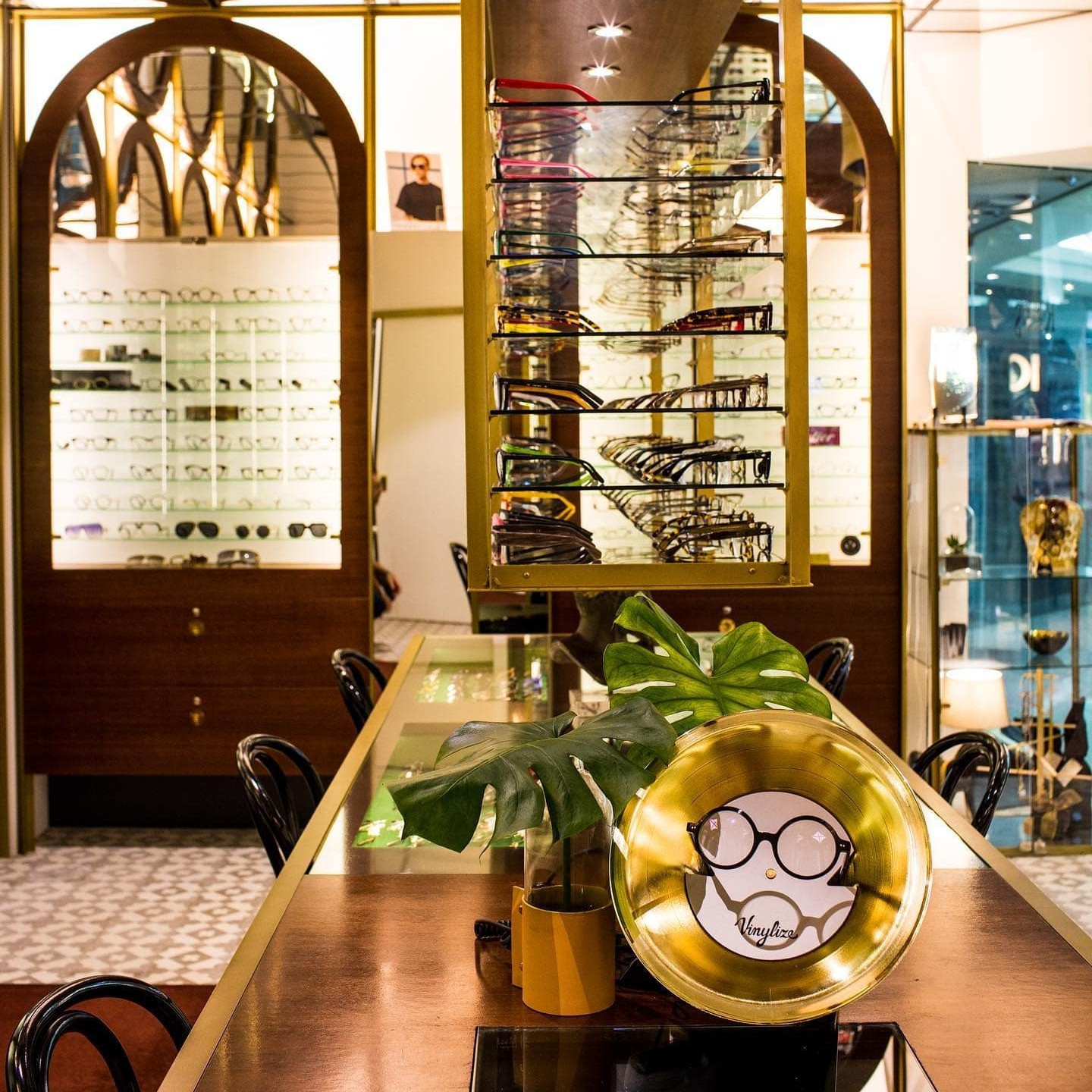 A Vinylize brand display featuring rows of eyeglasses on shelves and a gold decorative plate with an eyeglass logo on a central table.